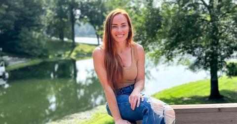 Mina Starsiak Hawk sits on a wooden deck, smiling in front of a river