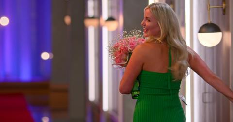 Laura, wearing a bright green halter dress, smiles over her shoulder as she carries a bouquet of flowers in Season 6 of 'Love Is Blind.'