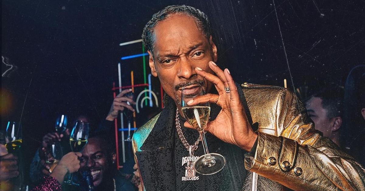 Snoop Dogg wears a black and gold blazer and a huge gold death row chain and drinks a glass of his 19 Crimes wine in the club.