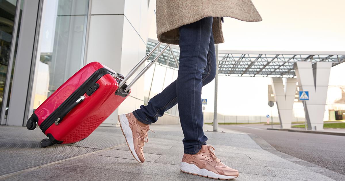 A person pulling a red suitcase outside an airport