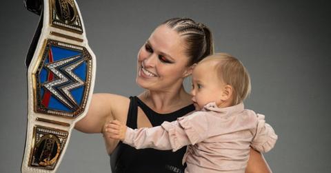 Ronda Rousey holding her daughter and a WWE championship belt