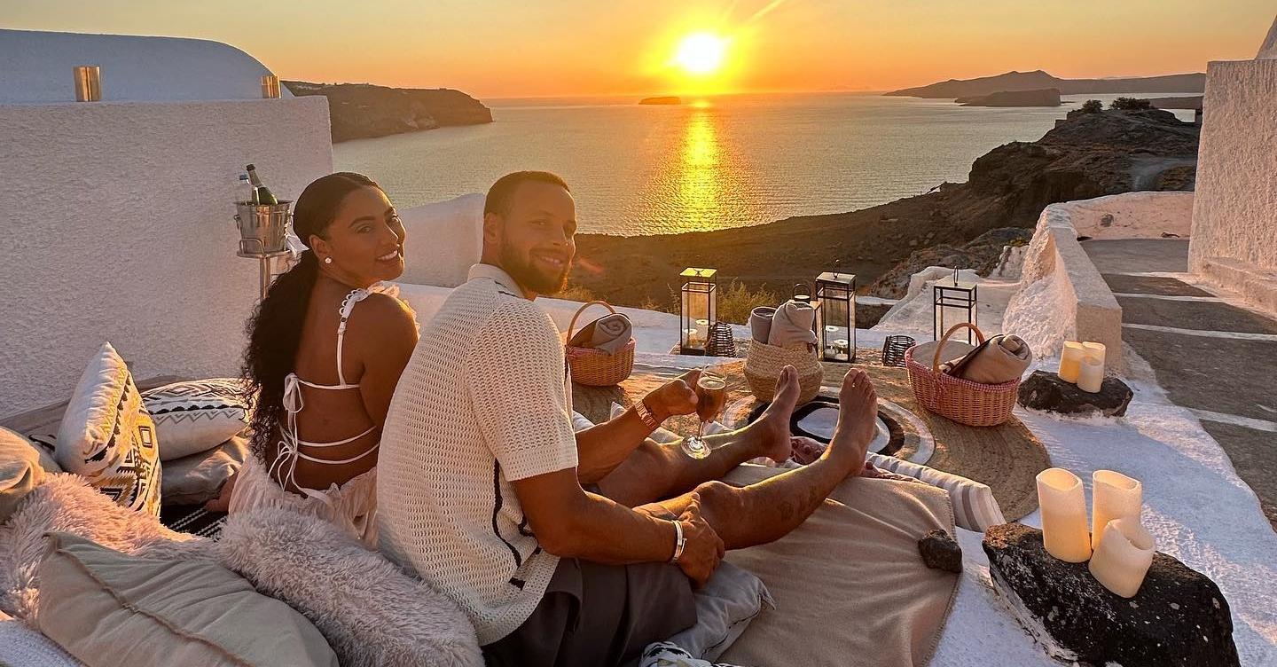 Ayesha and Steph curry have dinner overloocking the ocean while the sun sets.