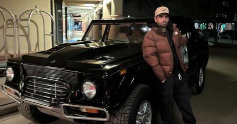 Scott Disick stands in front of his car wearing puffer jacket and hat