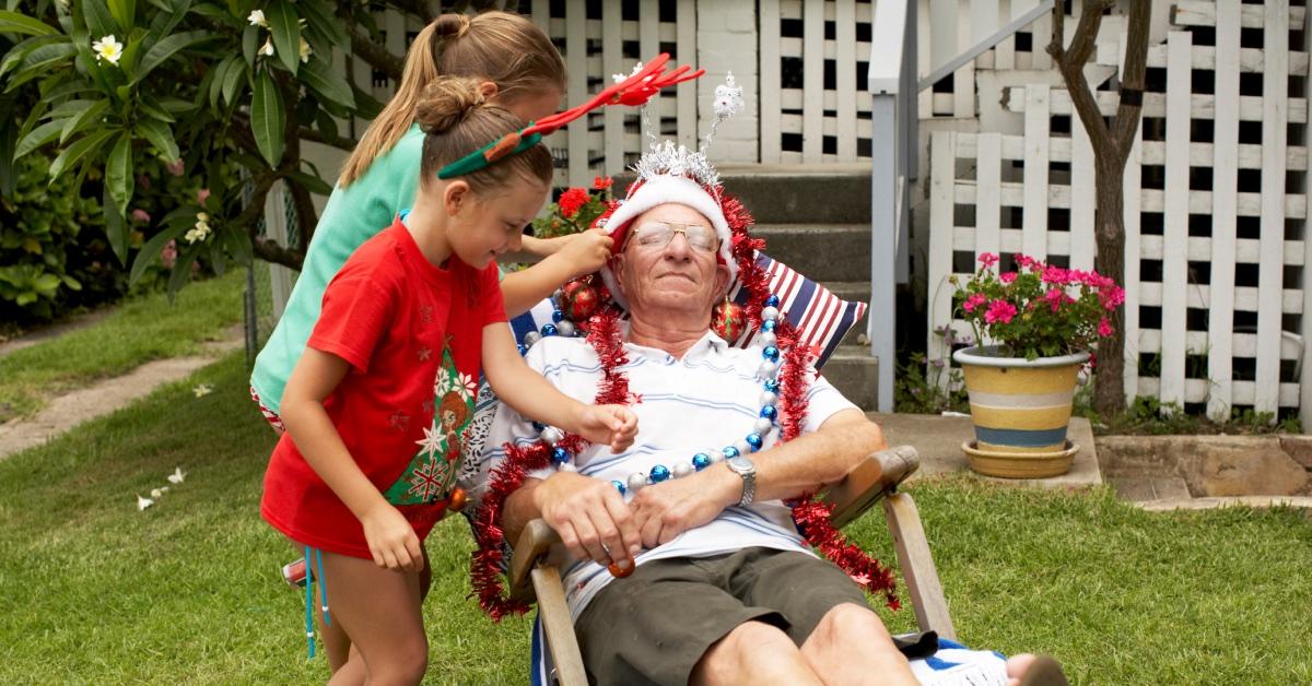 Two children putting Christmas decorations on an old man.