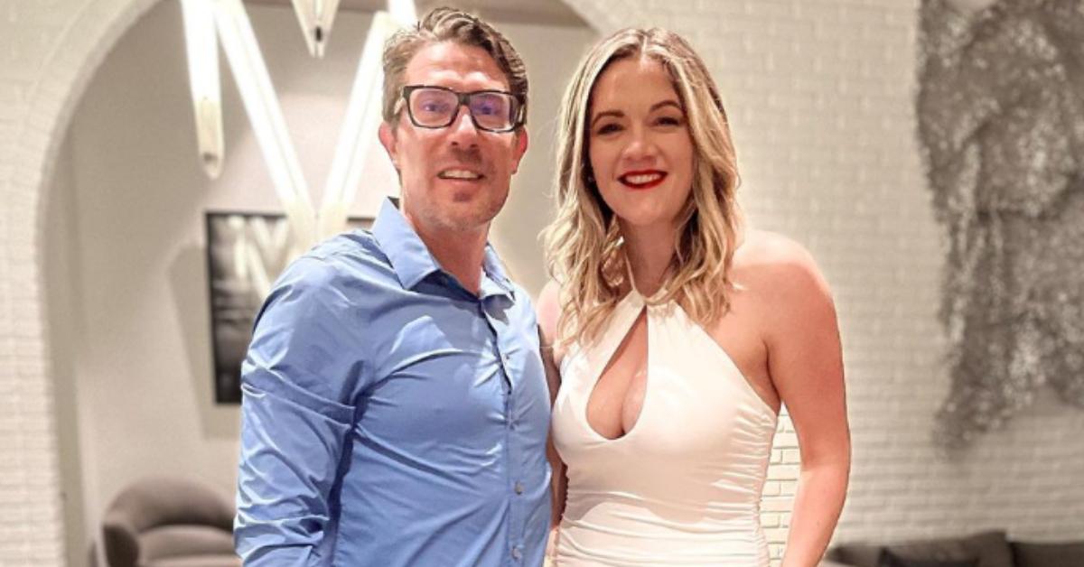 Garrick Merrifield wears a blue dress shirt and glasses as he poses alongside Dannielle, who dons a white high-neck cut-out minidress.