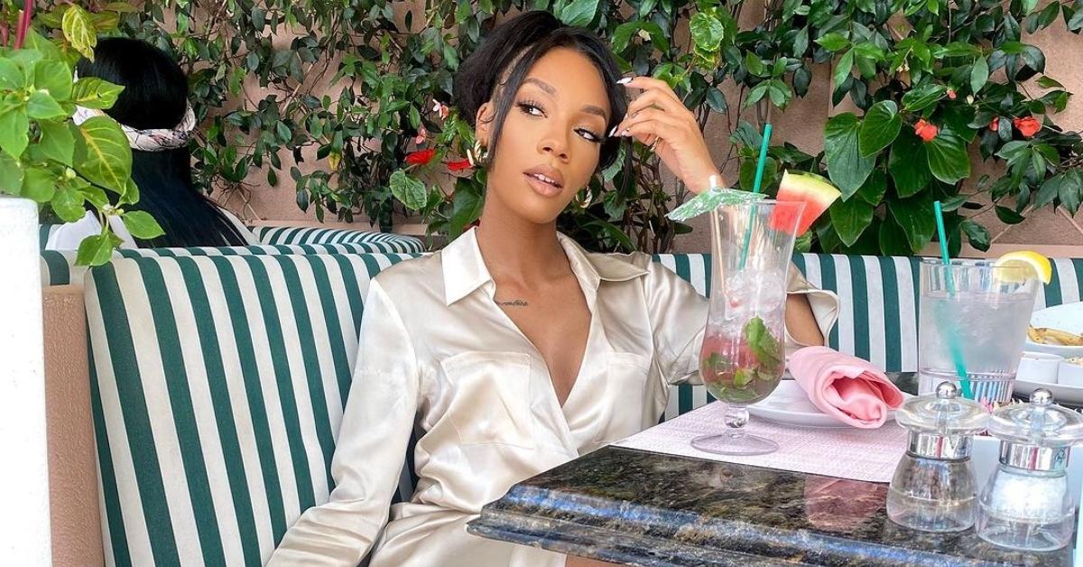 Kellie Sweet sits at brunch outside near plants in a satin robe.