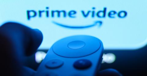 A person holding a remote control in front of screen with the Prime Video logo