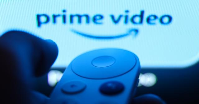 A person holding a remote control in front of screen with the Prime Video logo