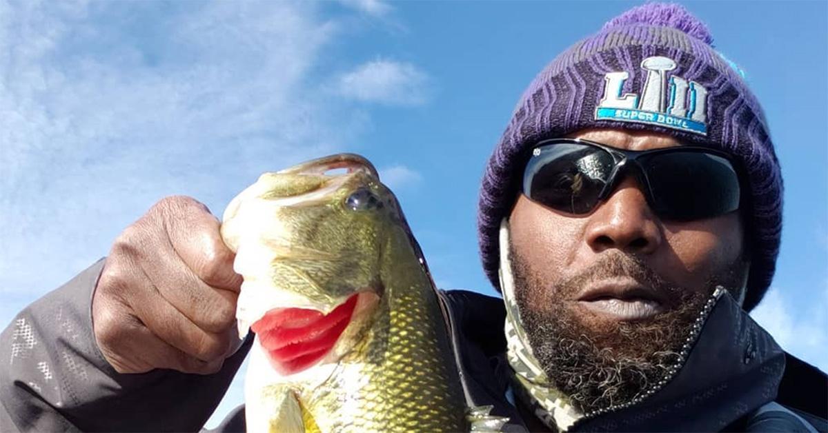 Randy Moss in a knit hat holding a fish. 