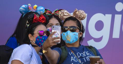 three women wearing mouse ears and masks take a selfie