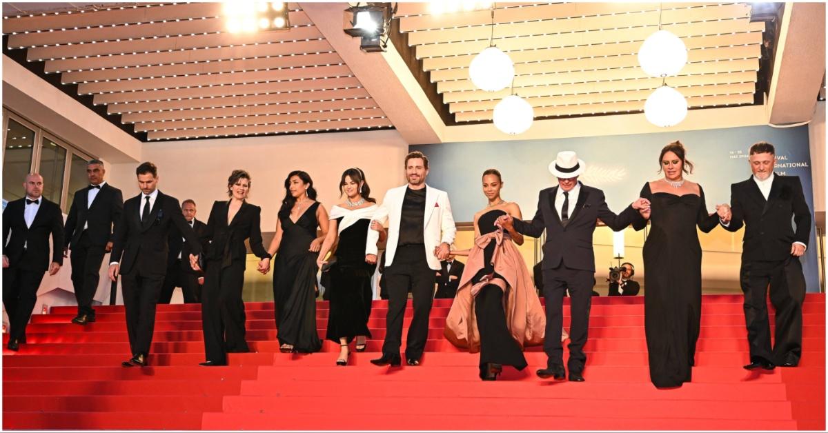 The cast of Emilia Pérez holding hands on red carpet stairs