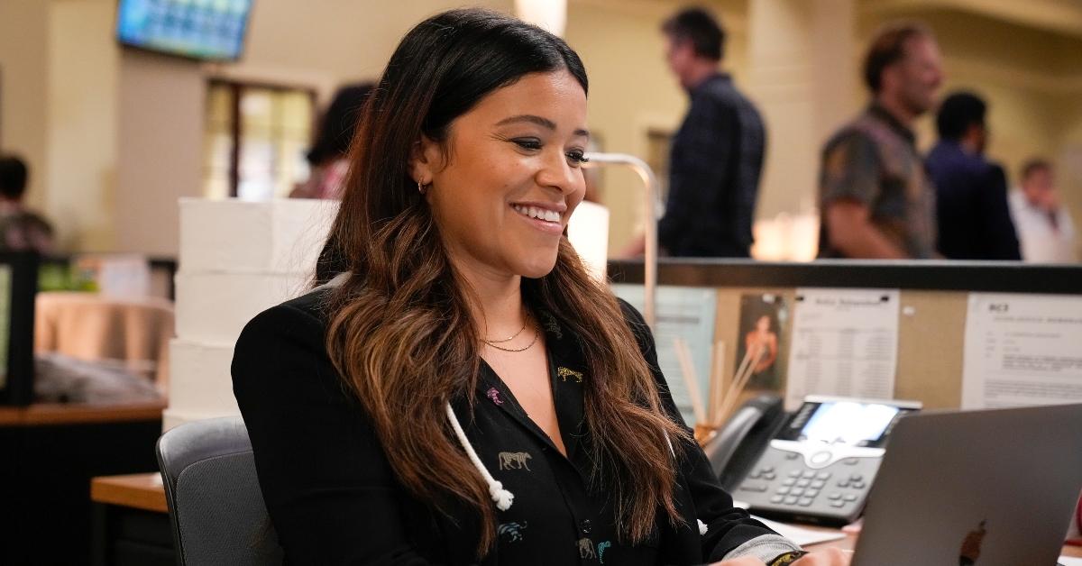 Gina Rodriguez as Nell smiling while typing on a computer in an office on ABC's 'Not Dead Yet'.