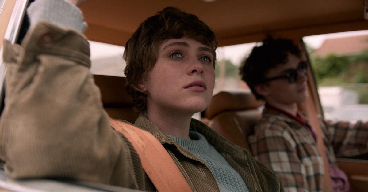 Sophia Lillis in I Am Not Okay Wit This. Sydney sits in the passenger seat of a cat, with her arm propped up on the open window. She gazes out of the window.