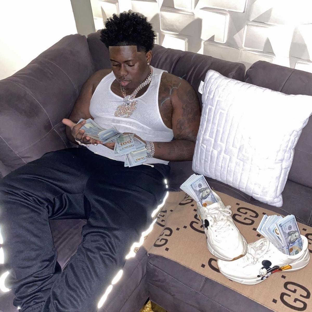 Sheff G sits on a couch with Gucci runner counting money