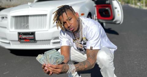 Rapper DDG poses with a stack of fanned out money wearing all white in front of a white Bentley with gold interior.