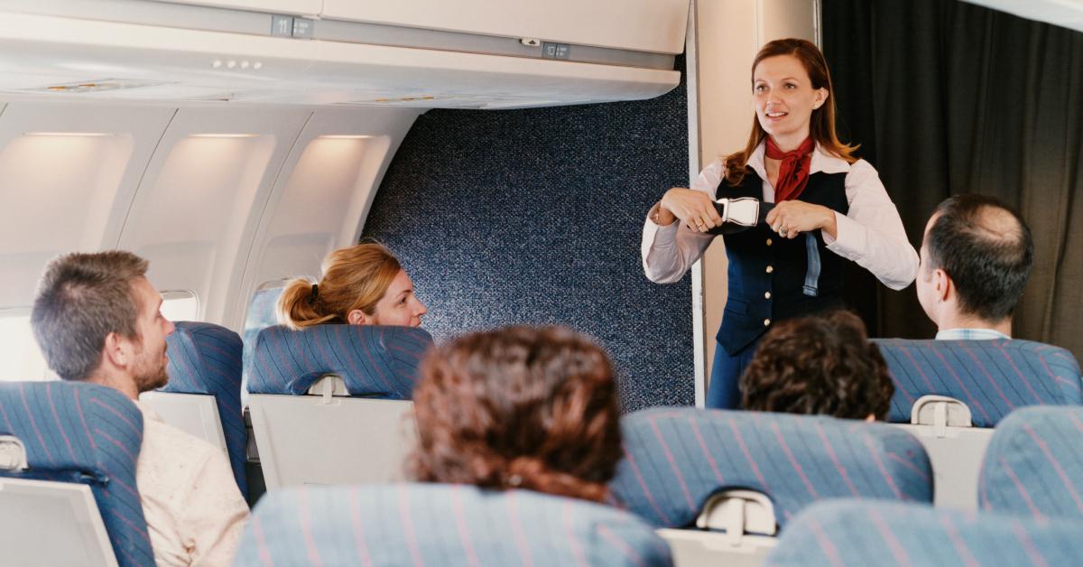 A female flight attendant demonstrates safety procedures for passengers.