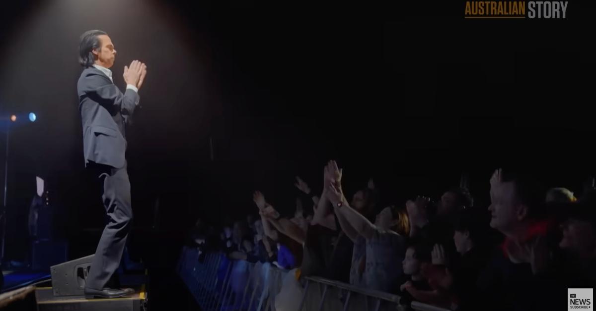 Nick Cave performing in 2024, clapping on stage in front of audience