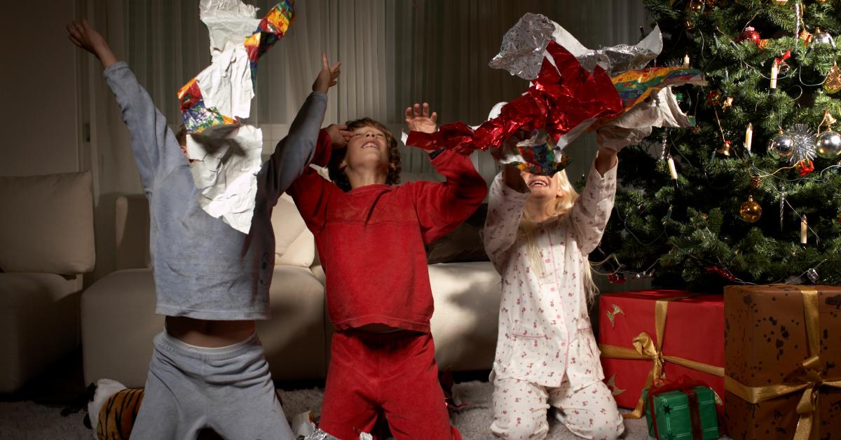 Three kids throw wrapping paper on Christmas morning.
