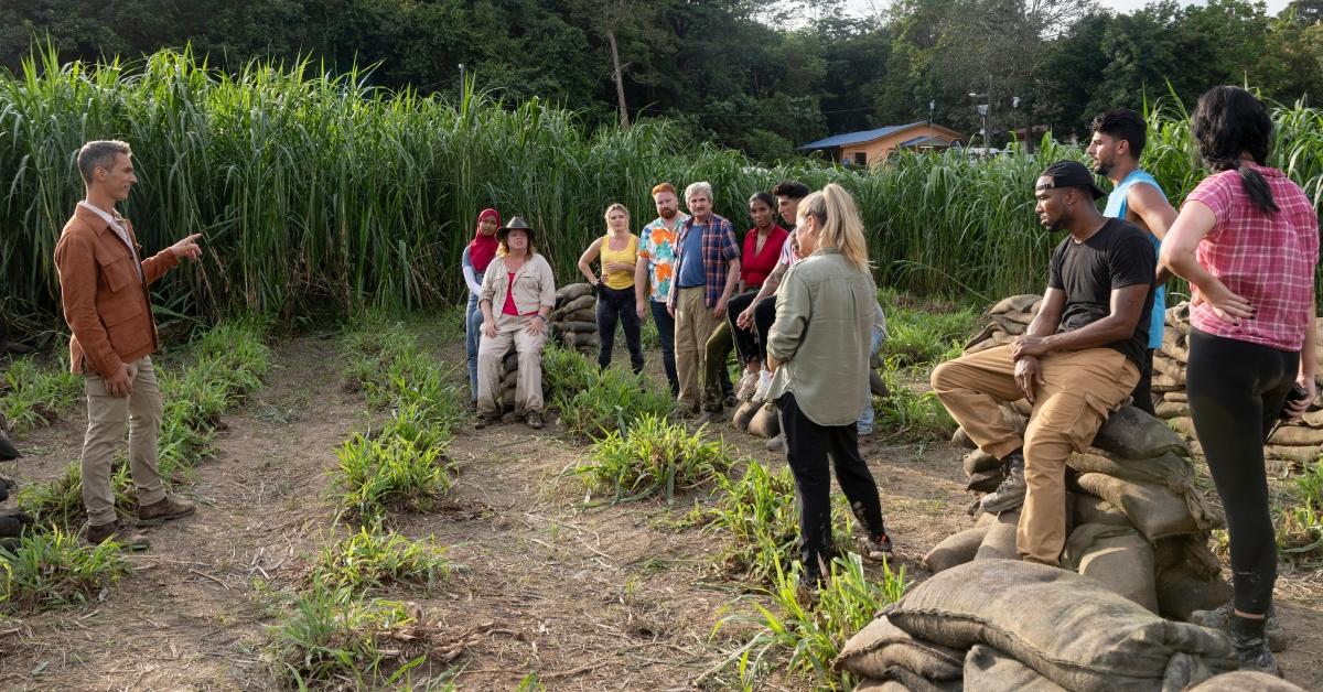 Host Ari Shapiro and the Season 2 cast of 'The Mole' chat in a field during Season 2, Episode 1.