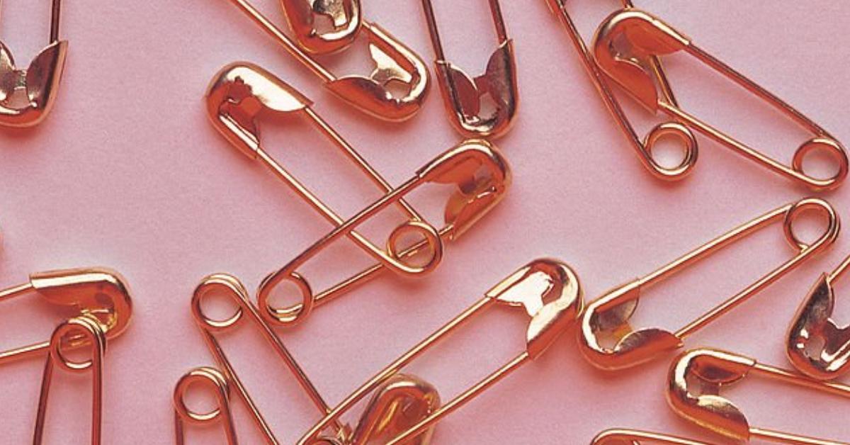 A pile of gold safety pins lay on a pink table.