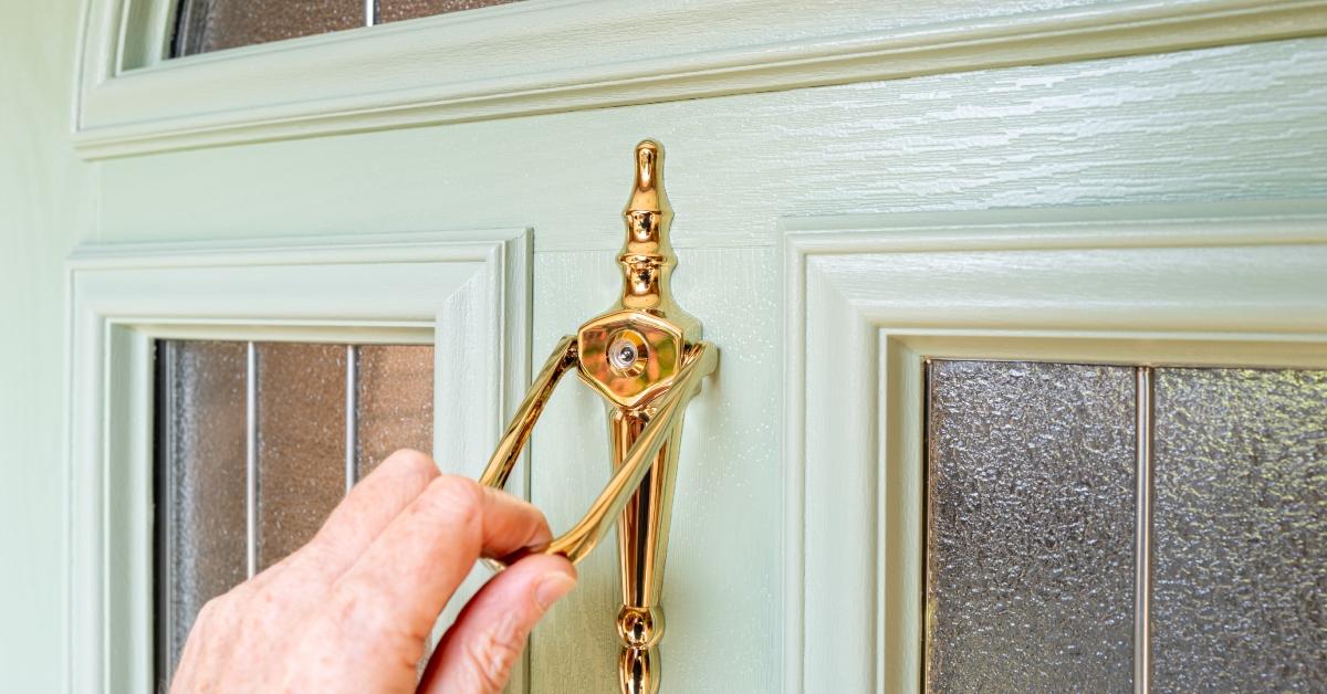 A person's hand is seen using the door knocker.