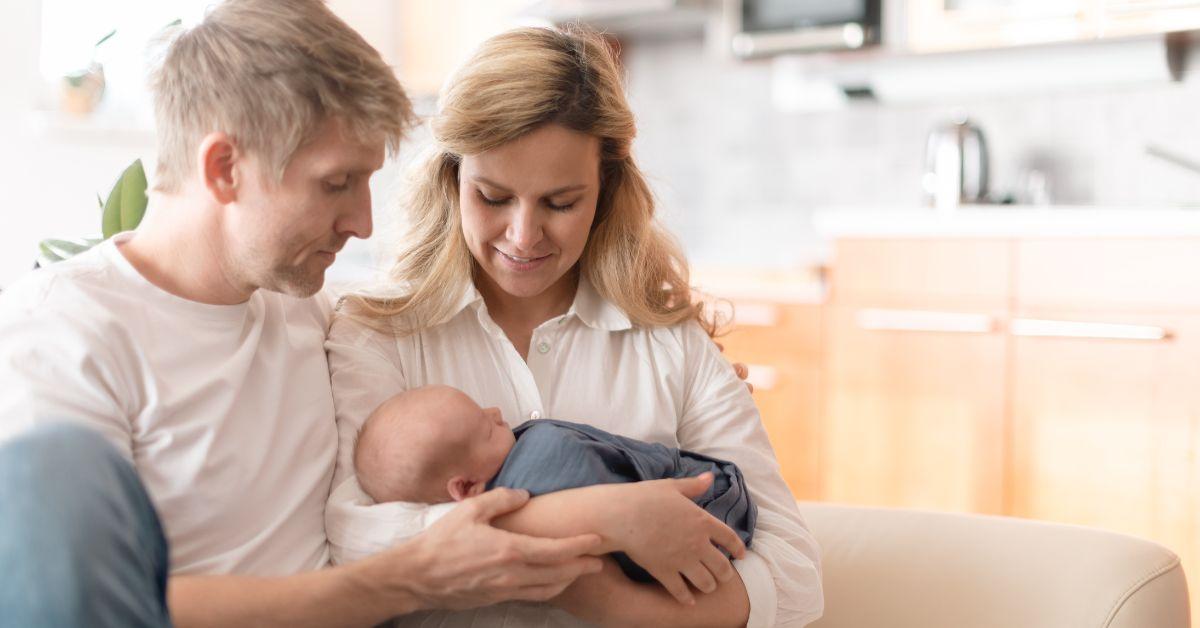 man and woman holding newborn baby on couch