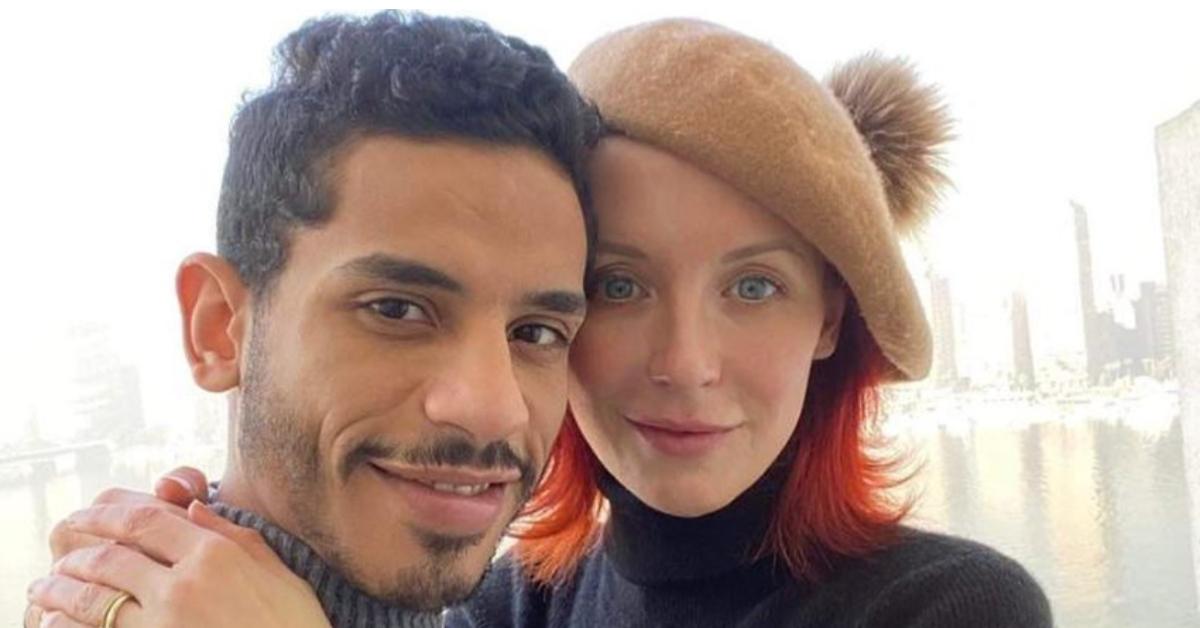 Mahmoud, wearing a gray turtleneck sweater, affectionately poses alongside his wife Nicole, who is dressed in a black turtleneck sweater and a tan-colored beret.