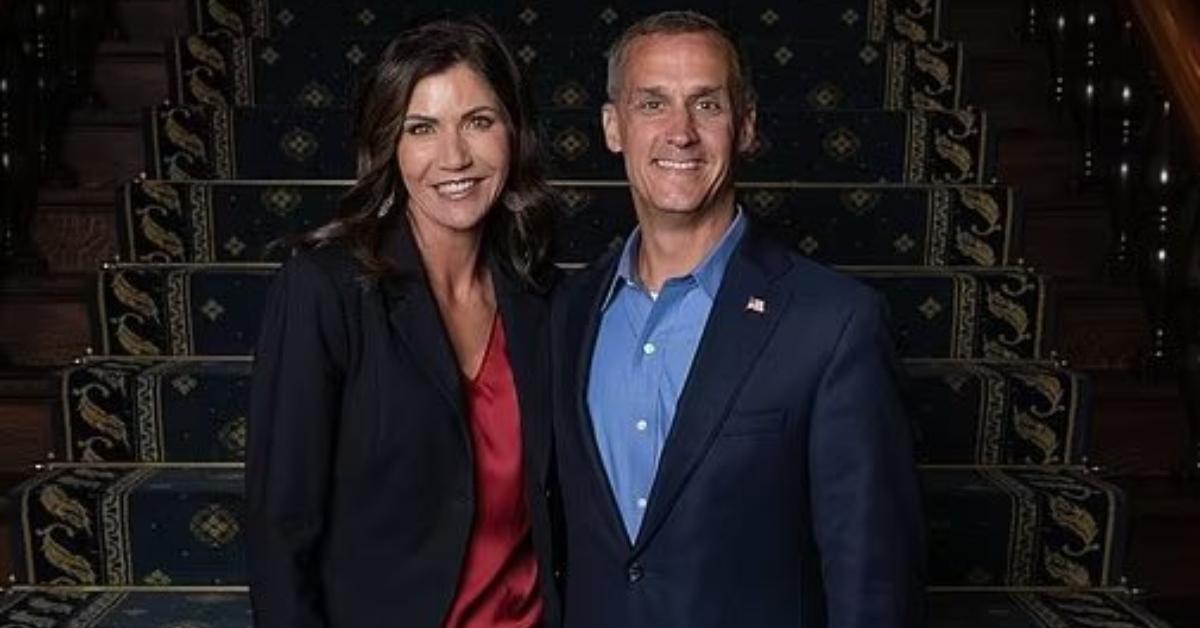 Kristi Noem and Corey Lewandowski pose by stairs together.