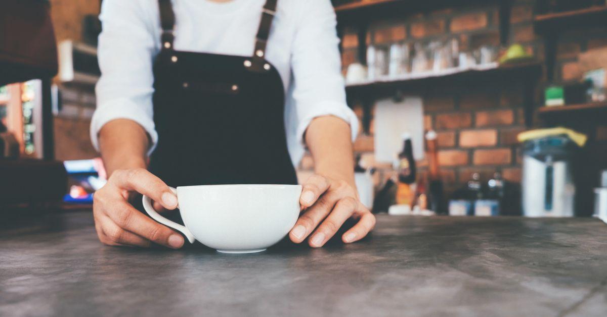 A barista holding a white teacup on a table.