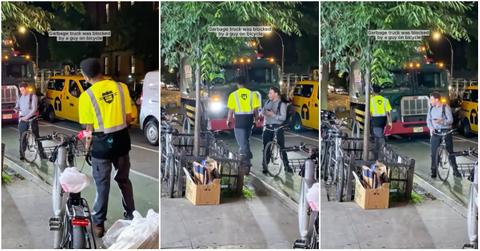 Biker sits in the road in front of a garbage truck intentionally blocking it from passing.