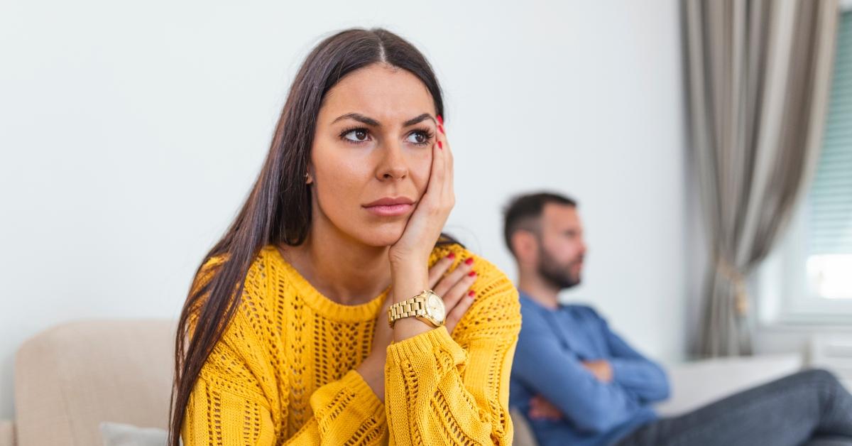 Woman looks annoyed as she sits on the couch with her husband.