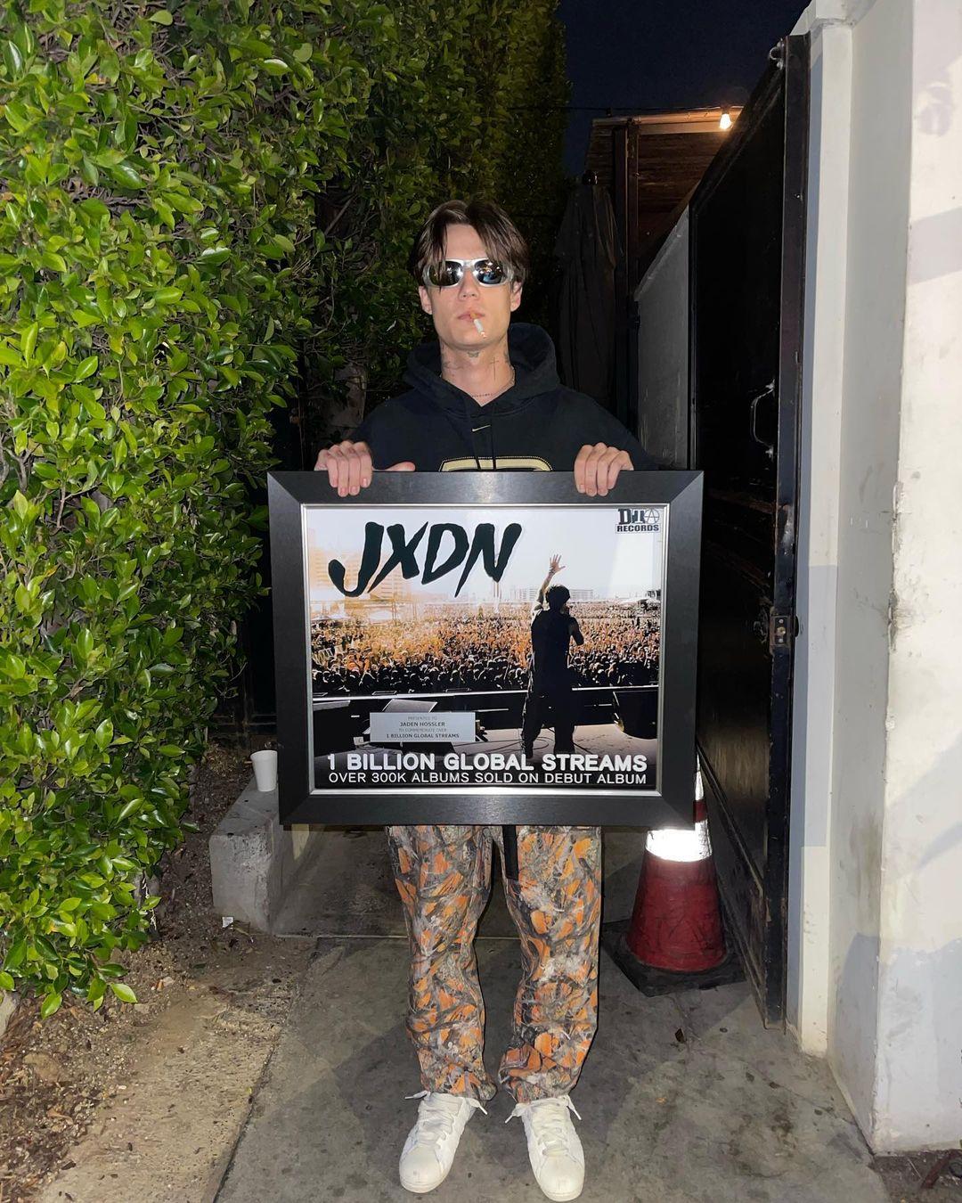 Jxdn seen holding a plaque for receiving over one billion global streams. In the upper right corner, Travis Barker's label is DTA Records is credited.