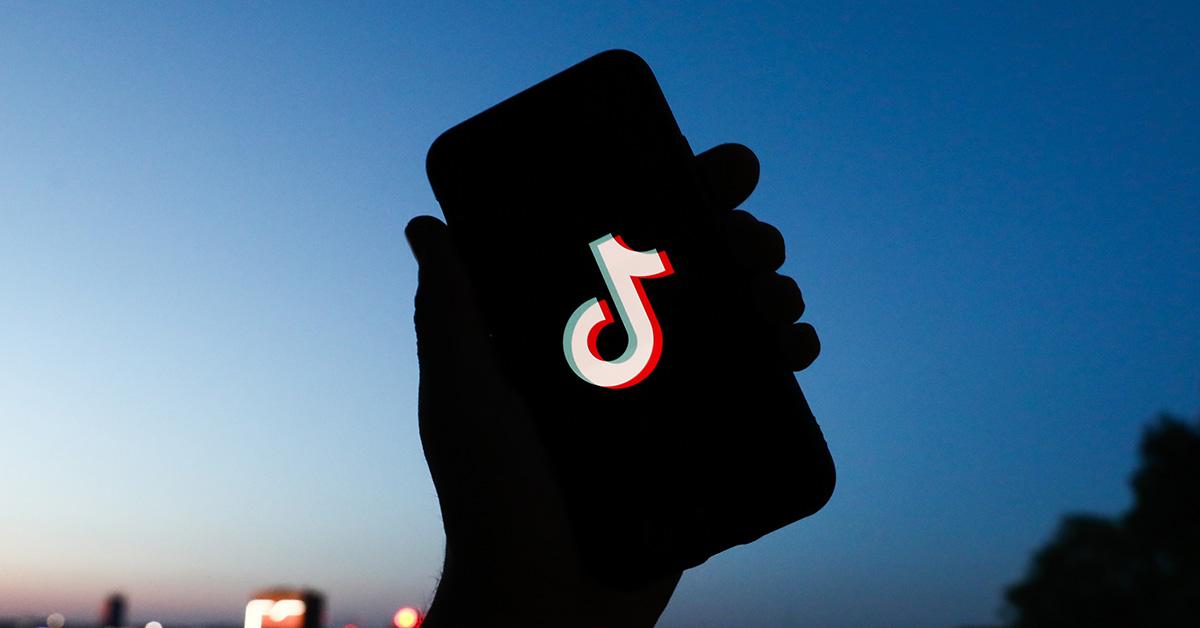 A hand holding a phone with the TikTok logo in silhouette.