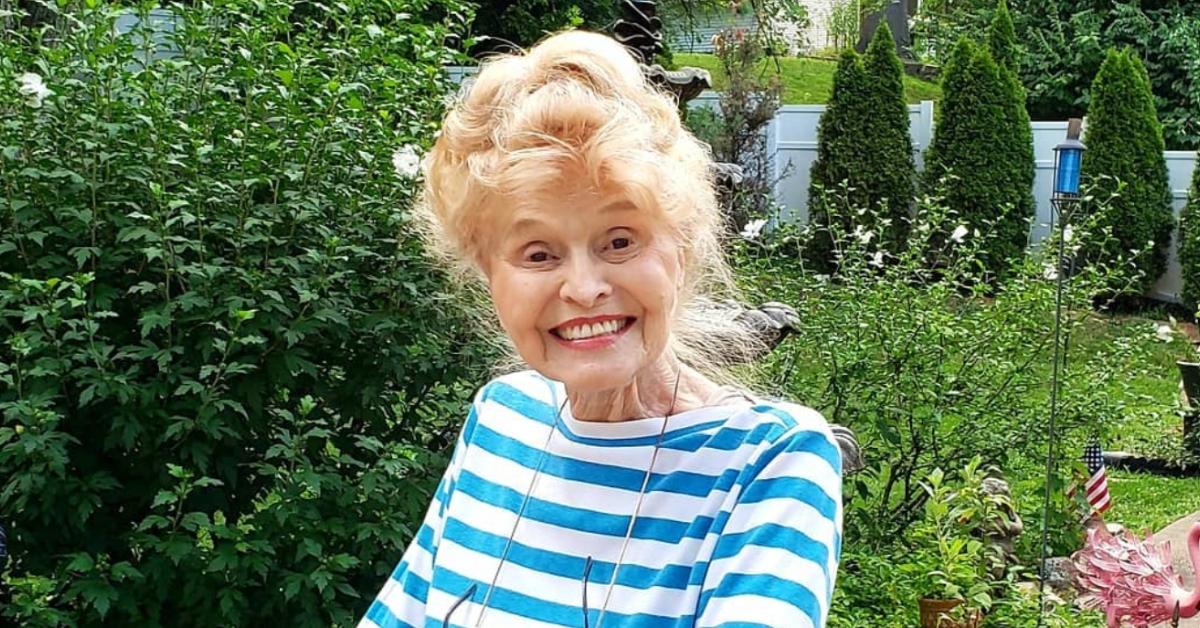 Mama Mai outside smiling in a blue and white striped shirt.