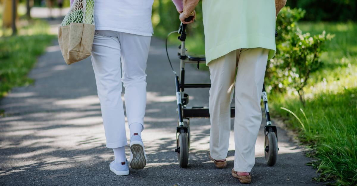An elderly person uses a walker to walk down a sidewalk.
