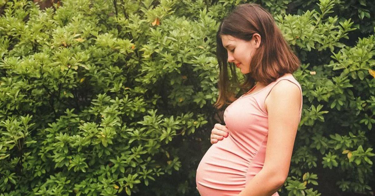 Priscilla Robertson holding her baby bump in a pink dress. 