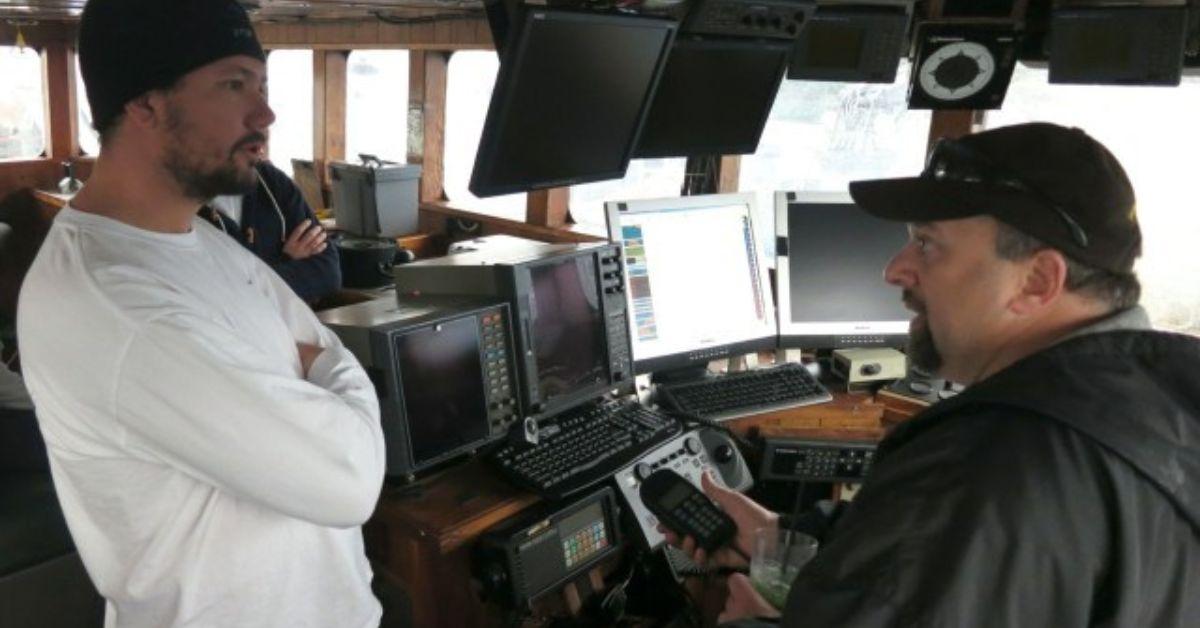 A crewman speaks with Tony Lara who is seated and holding the radio.