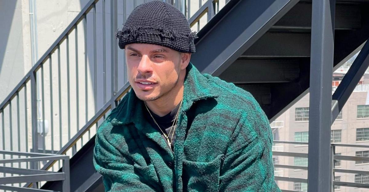 Beau Casper Smart posing in a green shirt and black hat near stairs.