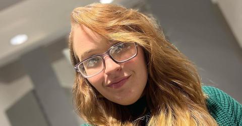 Anna wears glasses and a green sweater in a 2023 photo