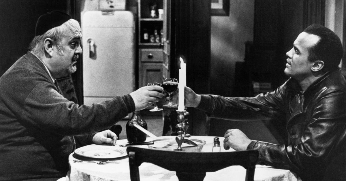 Zero Mostel and Harry Belafonte drink a glass of Passover wine together at a table in a scene from the film 'The Angel Levine,' 1970