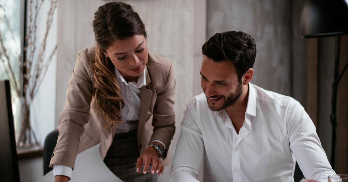 Female employee gets cozy with male co-worker who is smiling.