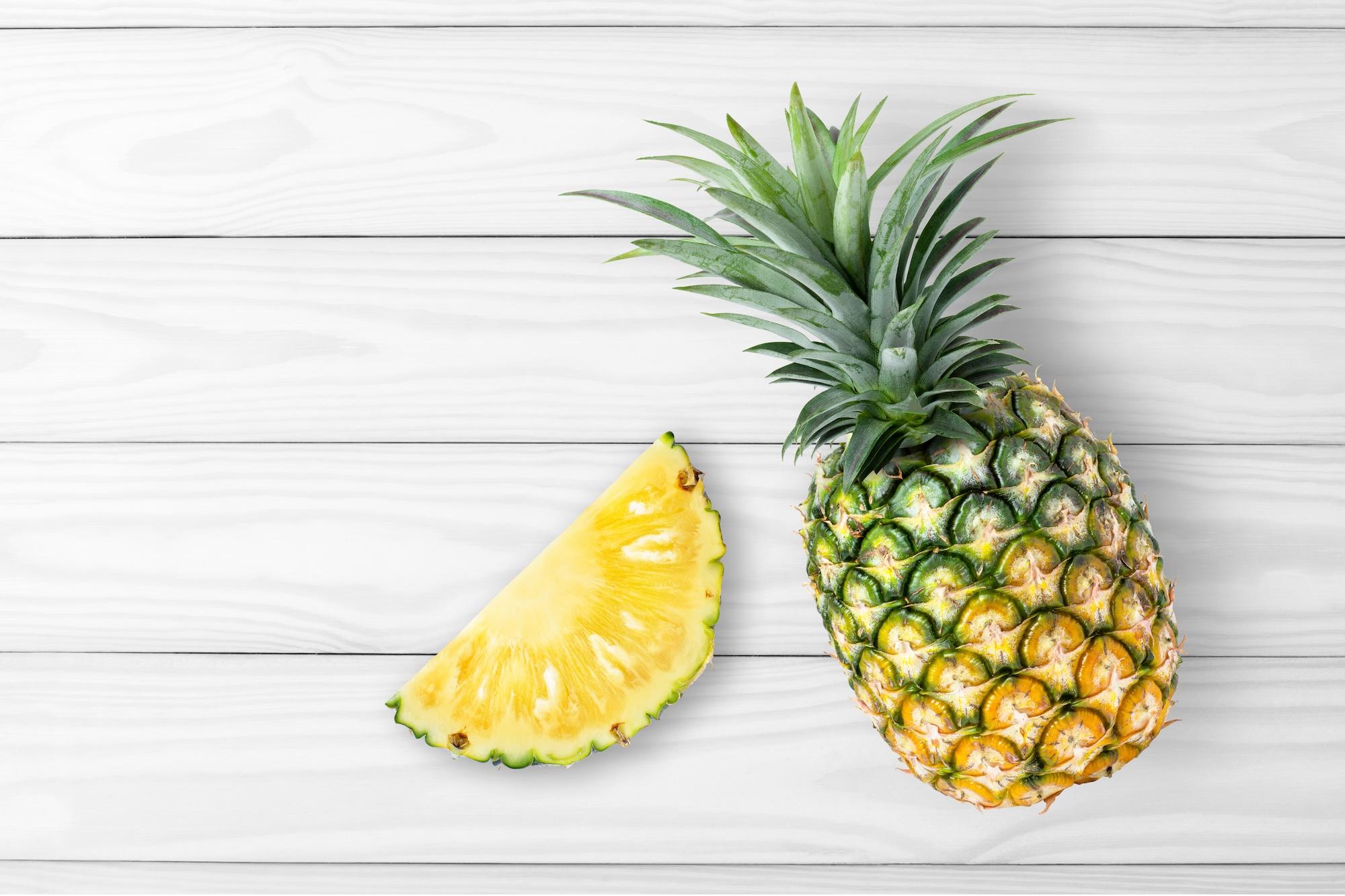 A whole pineapple and a slice of pineapple on wood table background