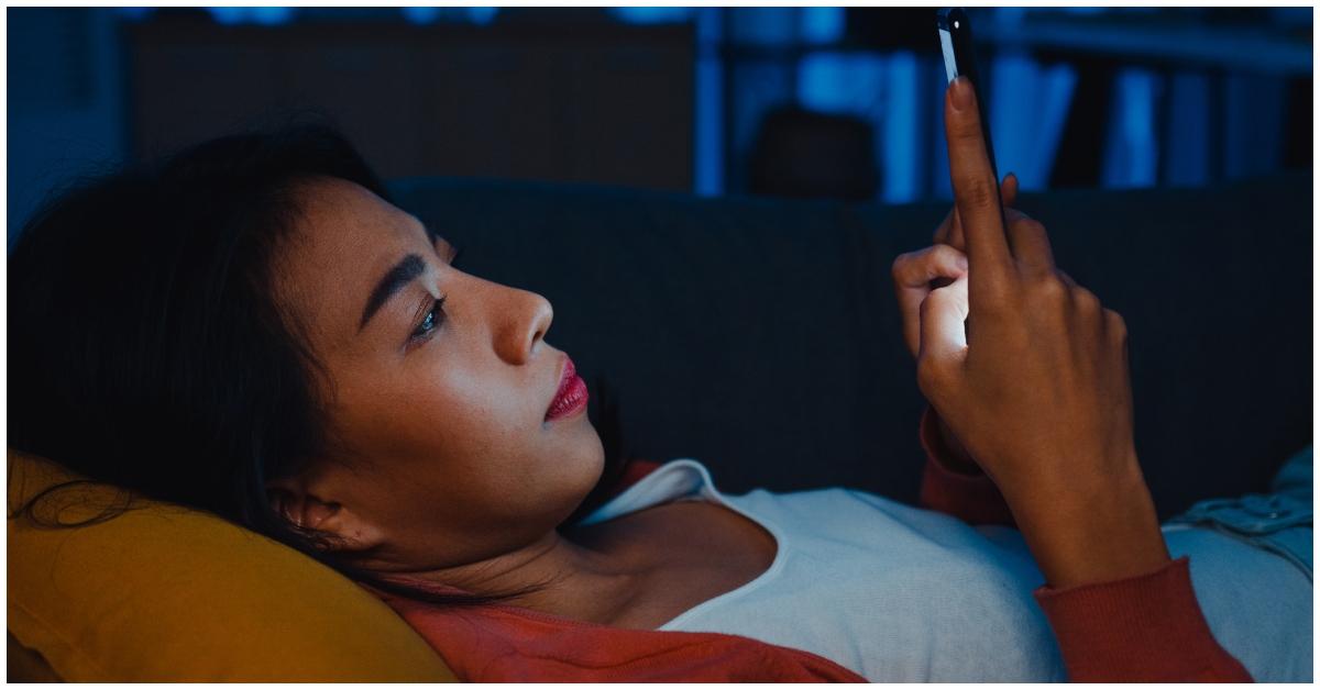 A woman looking at her phone while lying in bed.