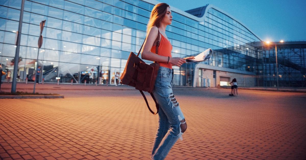Young woman traveling at night near the terminal of the airport or station and reading city map and looking for hotel - stock photo