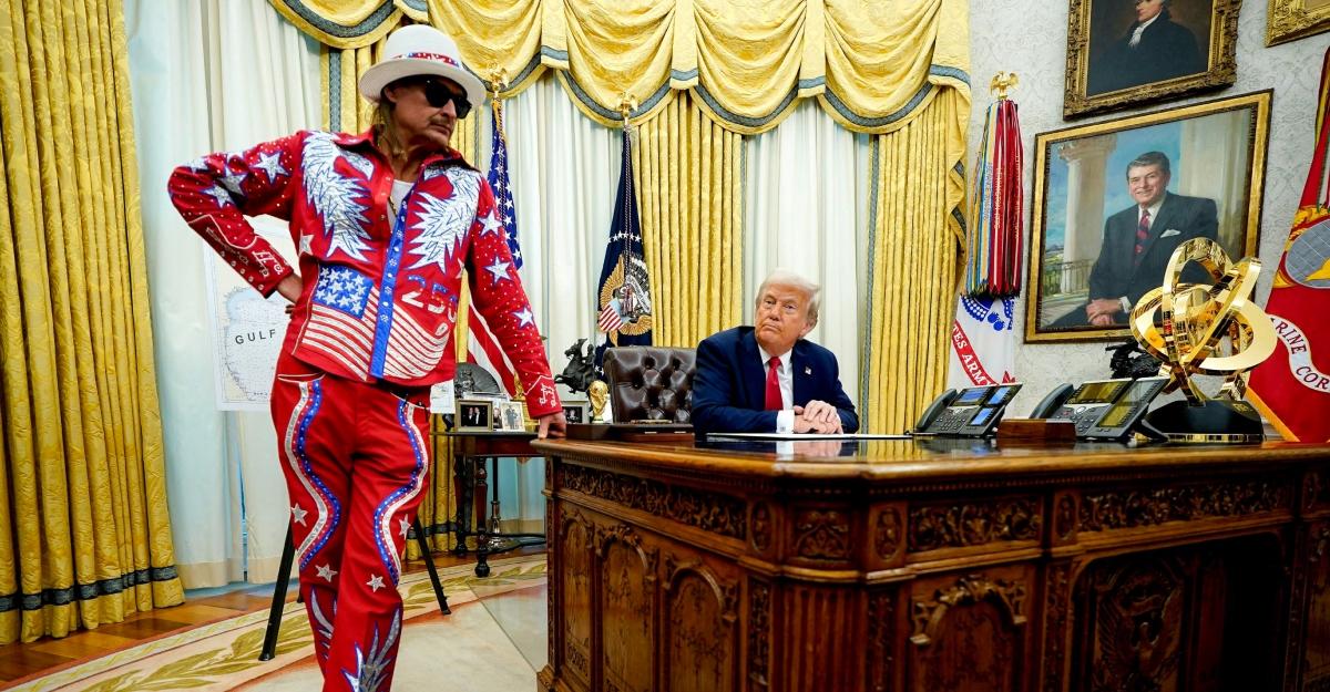 Kid Rock, dressed in red, white, and blue, leans on President Trump's desk in the Oval Office.