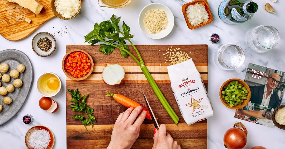 Photo of hands on a cutting board surrounded by ingredients for actor and filmmaker Stanley Tucci's S.Pellegrino 2023 recipe kit 