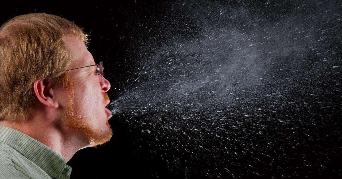 man sneezing and spraying saliva into the air