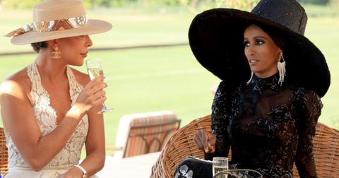 Taleen Marie and Chanel Ayan seated outside and speaking to each other while wearing large hats