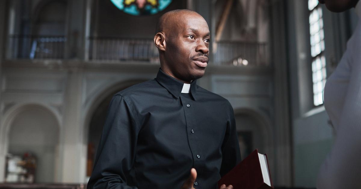 Black astor in religious garb talks to woman at church. 