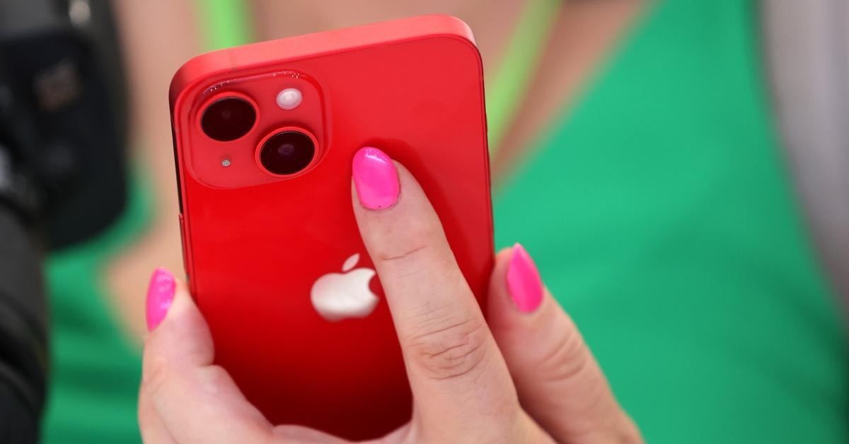 woman with pink nails and green shirt holds red iphone in her hands